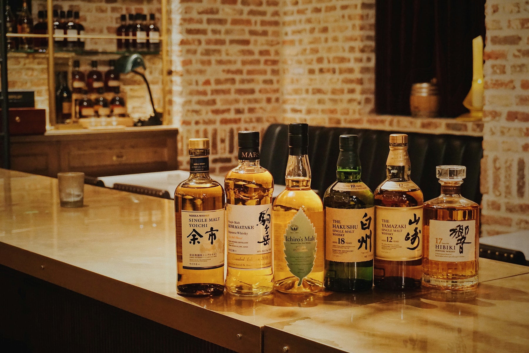 Assorted Japanese whisky bottles displayed on a bar, including Yamazaki, Hakushu and Hibiki